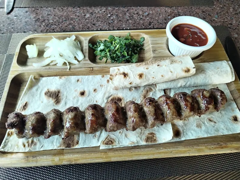 Kebab on lavash with onion, herbs and tomato sauce on a wooden board